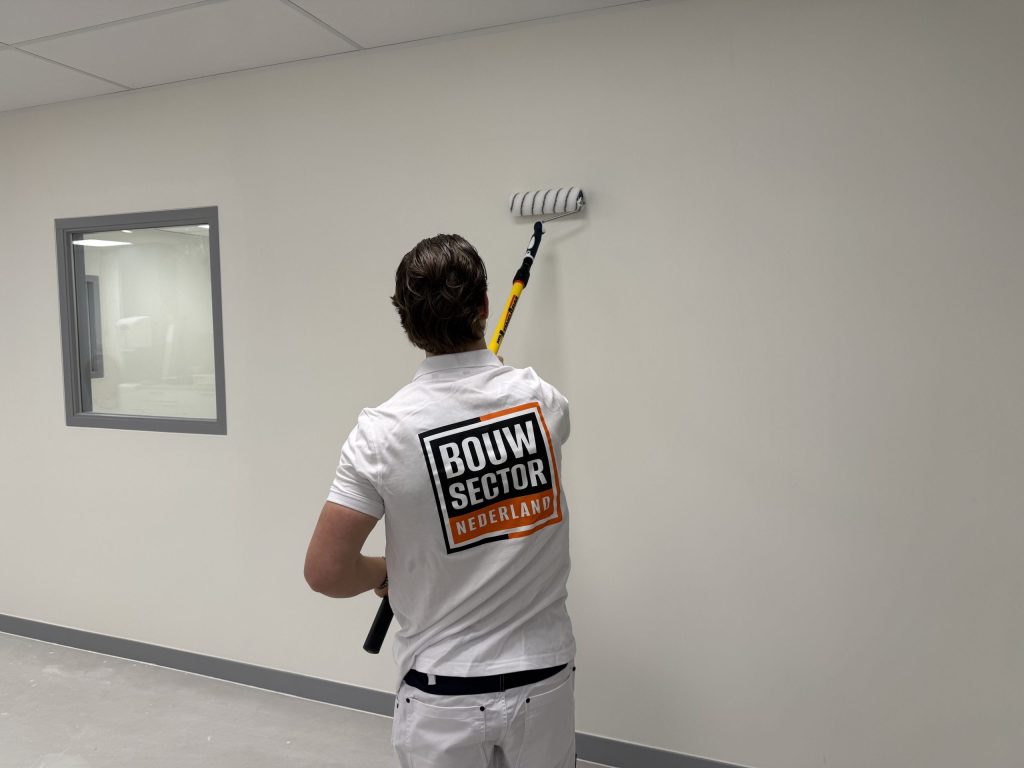 Schilder rolt een lichte muur in een ruimte met een binnenraam in een grijs kozijn