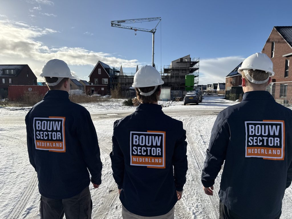 Drie vakmensen van Bouwsector Nederland met witte helm voor een rij woningen in aanbouw
