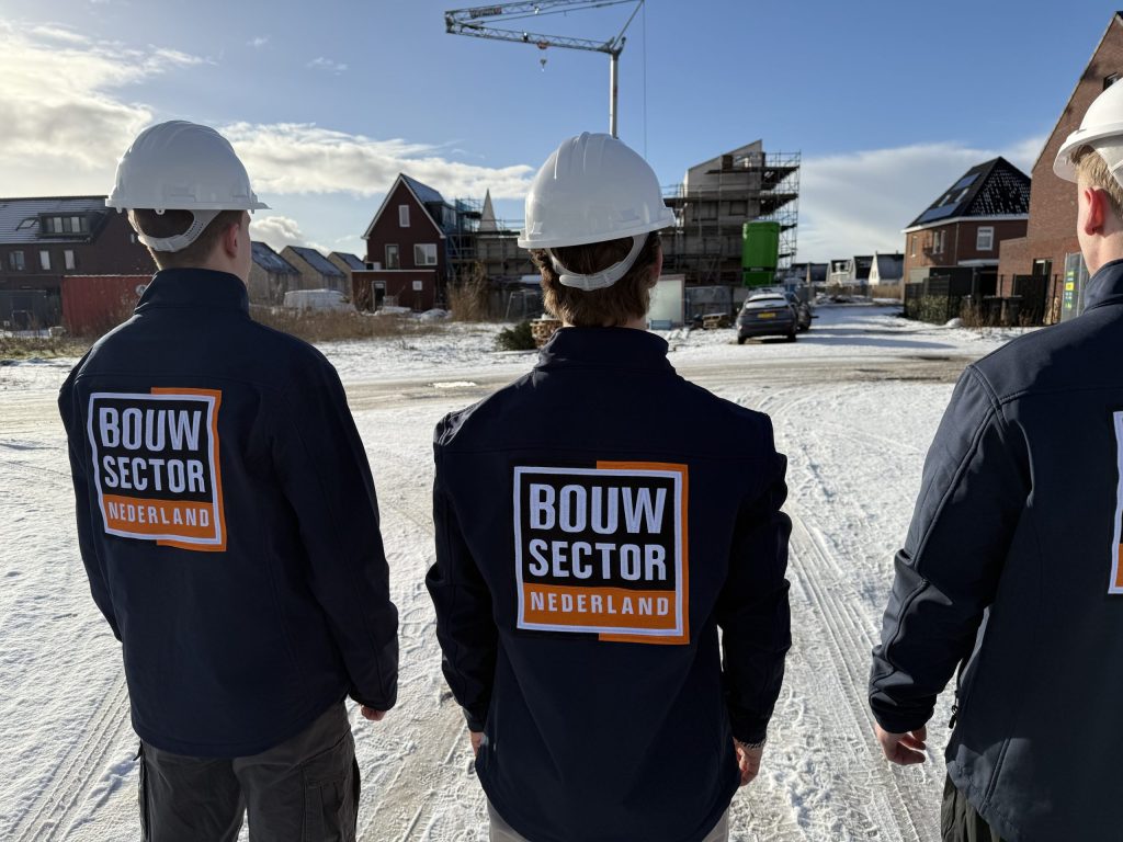 Drie vakmensen in jassen van Bouwsector Nederland met witte helm kijken naar nieuwbouwwoningen