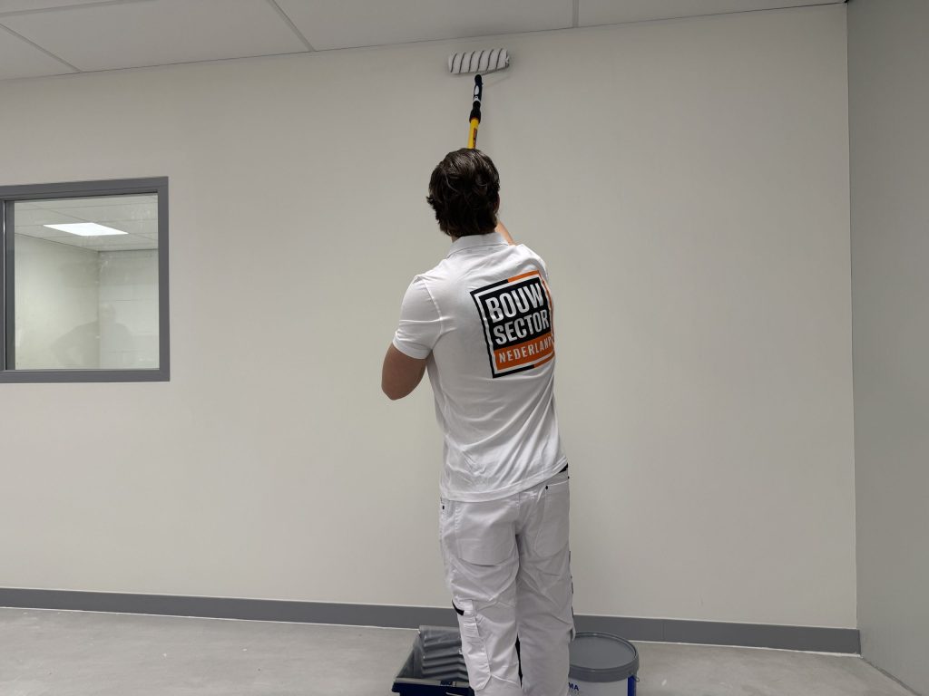 Schilder in wit tenue rolt het bovenste deel van een lege wand