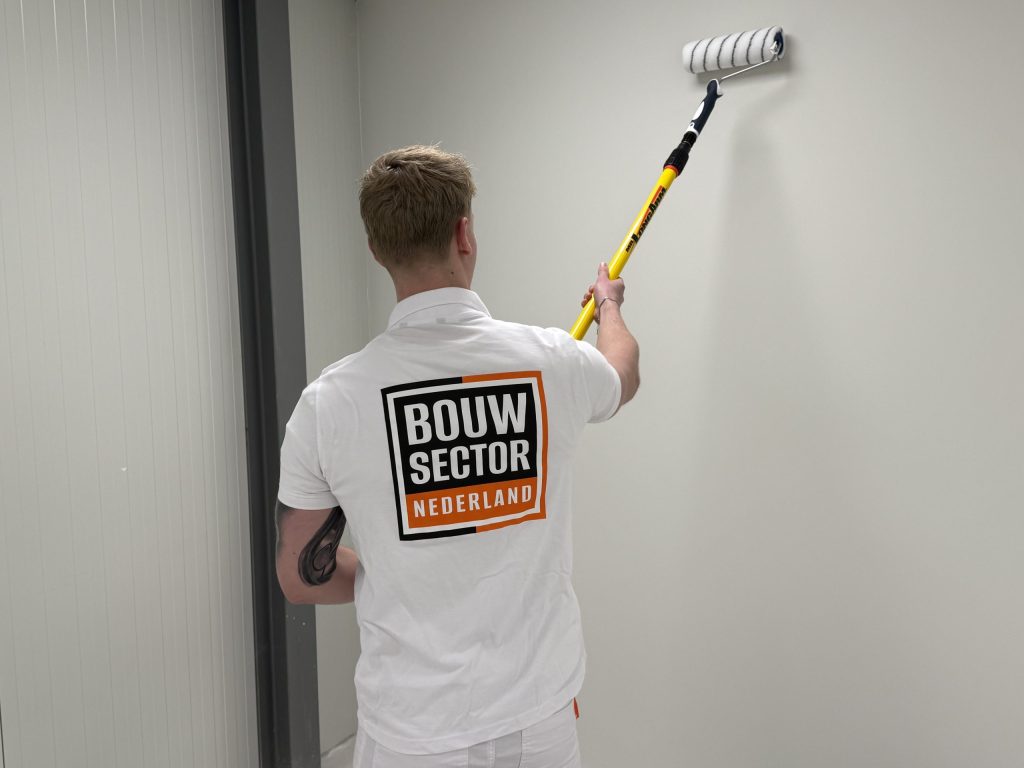 Schilder van Bouwsector Nederland zet een lichte wand in de verf naast een wand van verticale panelen