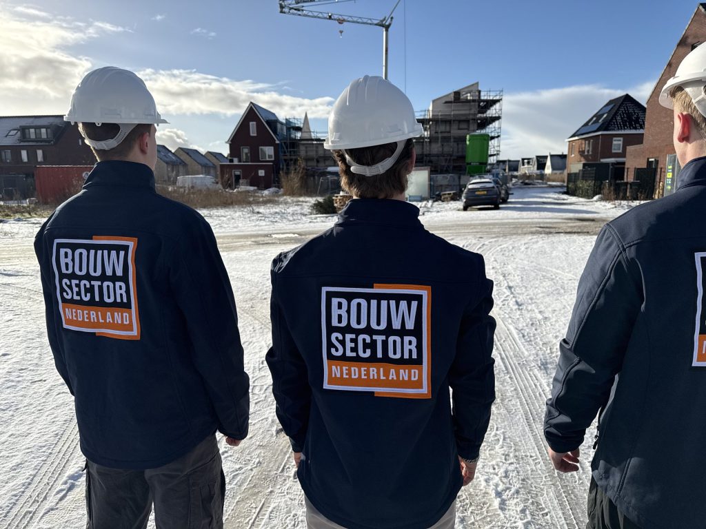 Drie mannen in werkjas met het logo van Bouwsector Nederland voor een rij huizen